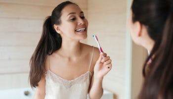 A happy Asian woman looking at her reflection in the mirror while brushing her teeth.