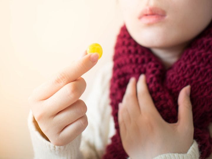 Woman holding a yellow-coloured lozenge with her right thumb and index finger.  
