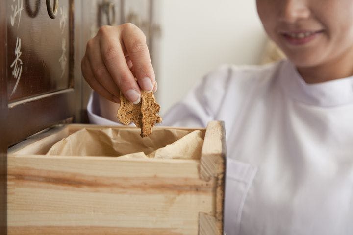TCM professional picks out a few dried herbs from an apothecary drawer.