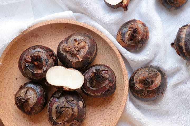 Close-up display of water chestnuts in a wooden tray and on a white cloth.