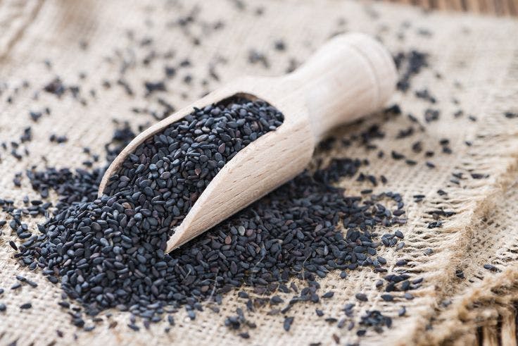 Black sesame seeds in a wooden scoop and on burlap.