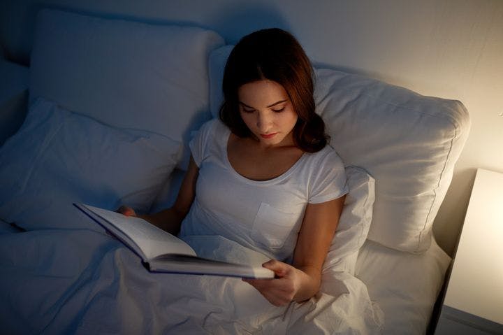 A woman reading book on a bed.
