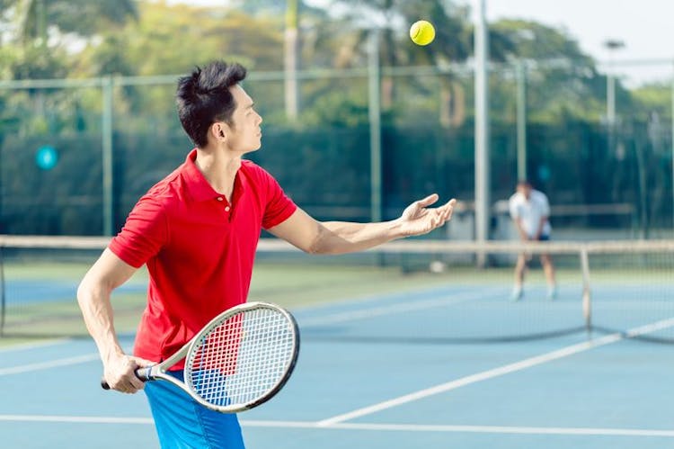 Man in red polo shirt playing tennis outdoors. 
