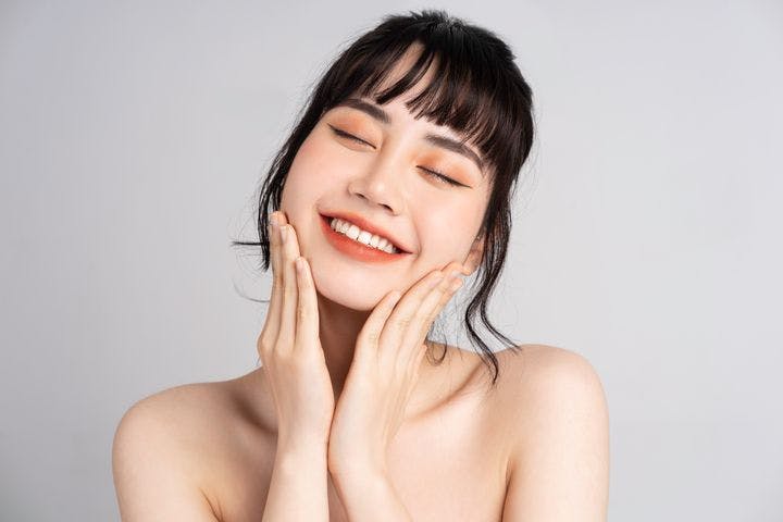 A portrait of a happy, young Asian woman touching her face.