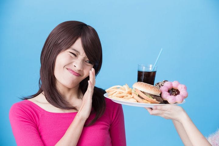 Woman scrunching her face while turning away a plate of unhealthy foods and a cup of cola with her left palm.