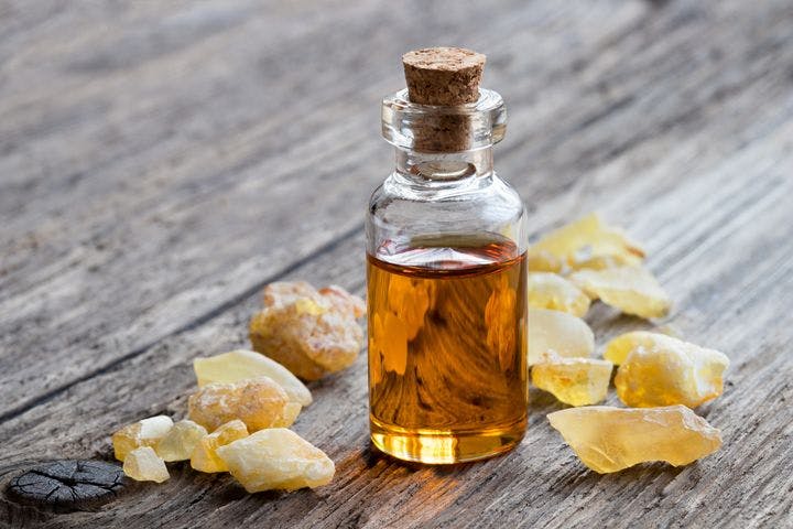 Frankincense oil in a bottle with frankincense resin surrounding it on a wooden table.