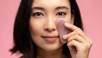 Closeup pic of Asian woman enjoying gua sha benefits on face, isolated against pink background