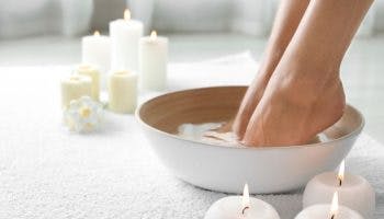 A woman soaking her feet in a bowl of warm water set on a white towel surrounded by candles.