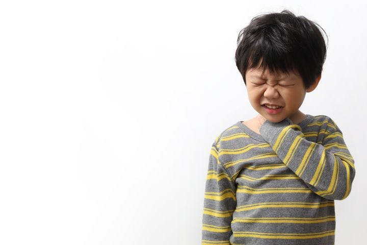 A boy grimacing in pain while holding his throat with his left hand. 