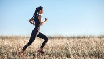 An Asian woman working out by running across a field.