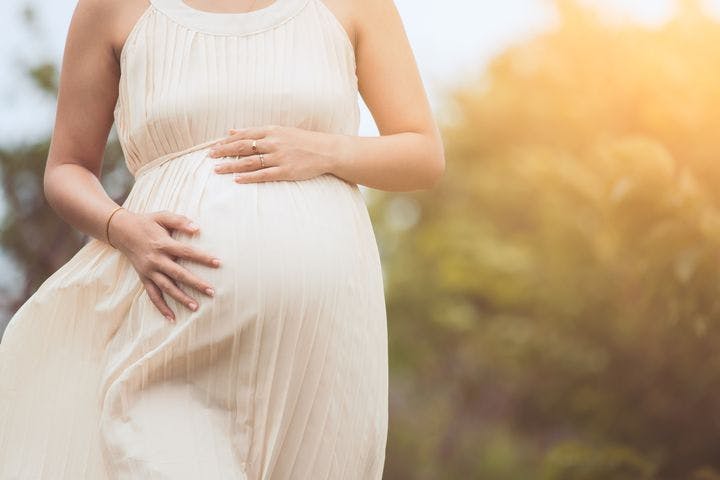 Pregnant woman with her hands on her belly and walking outdoors.