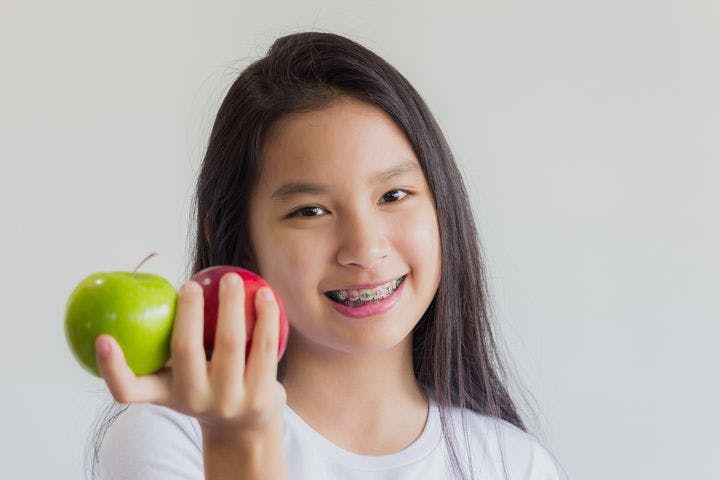 Early teen girl smiles while holding a green apple and a red apple in her hand.