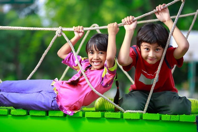 Young girl and boy smile while playing in a playground outdoors.