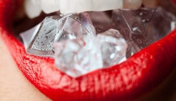 Close-up of a woman’s lips in red lipstick as she bites a few ice cubes. 