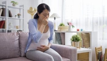 Young expecting mother on sofa, suffering from pregnancy nausea