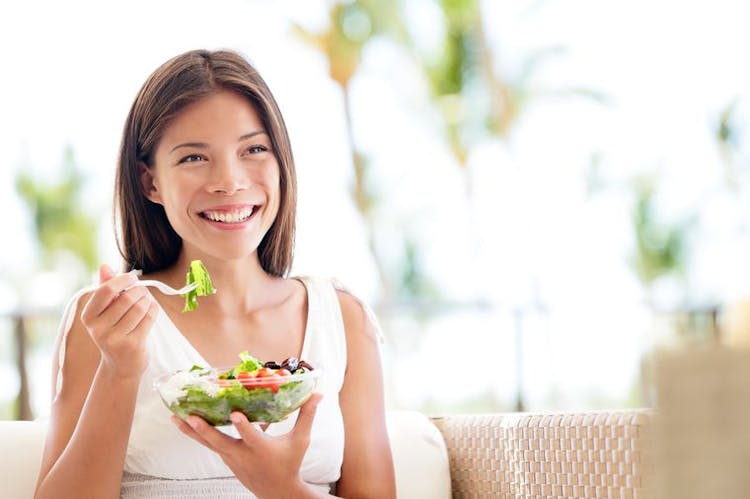 Woman holds a clear bowl of salad and a fork in one hand.
