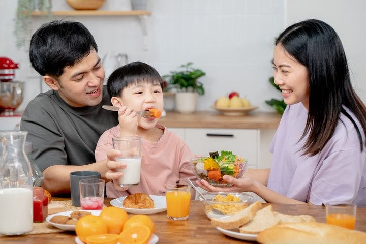 Asian parents having breakfast with their young son in a kitchen.
