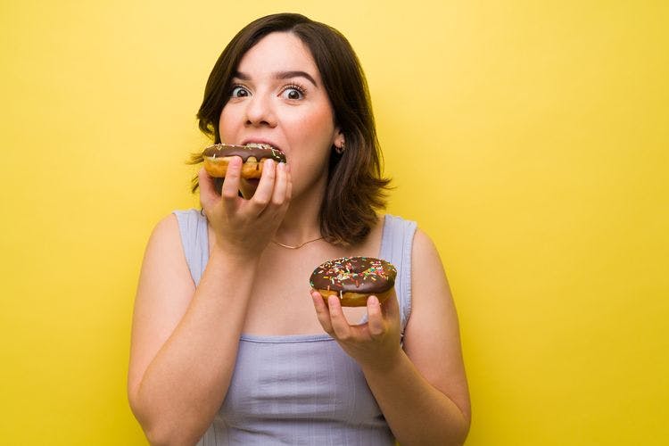 Woman holding a doughnut in one hand and eating another doughnut in the other.