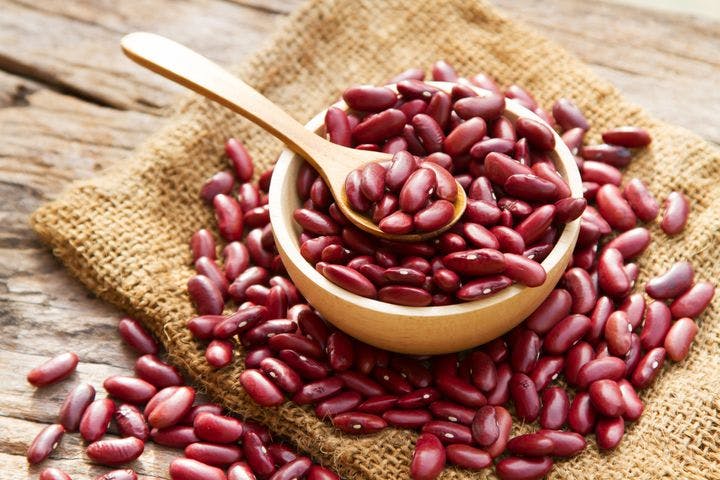 Red kidney beans in a wooden bowl, spoon and scattered on a mat
