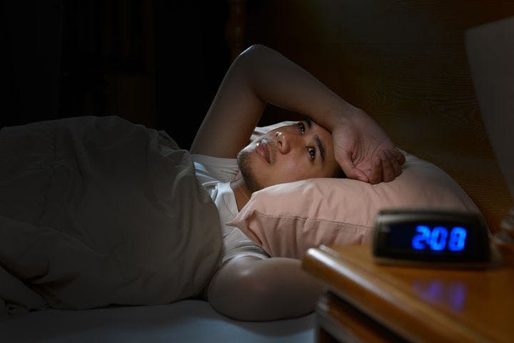 Man lying awake in bed, unable to sleep due to insomnia and a digital clock showing 2.08am.