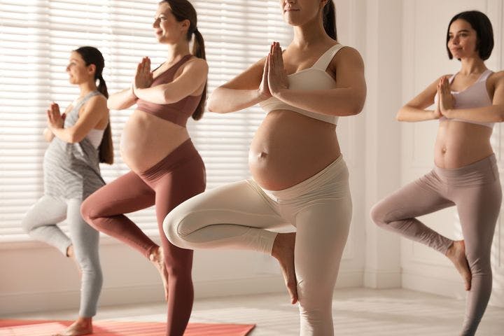Four pregnant women performing a yoga standing tree pose.
