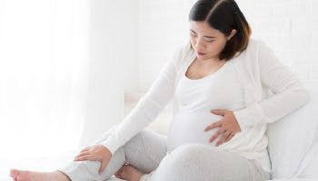 Pregnant woman sitting and holding her stomach and leg.