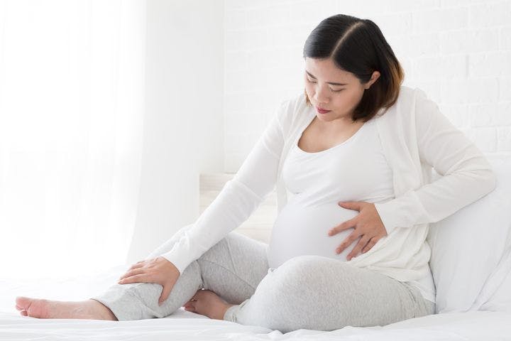 Pregnant woman sitting and holding her stomach and leg.