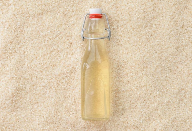 A bottle of rice vinegar lying on a bed of rice.