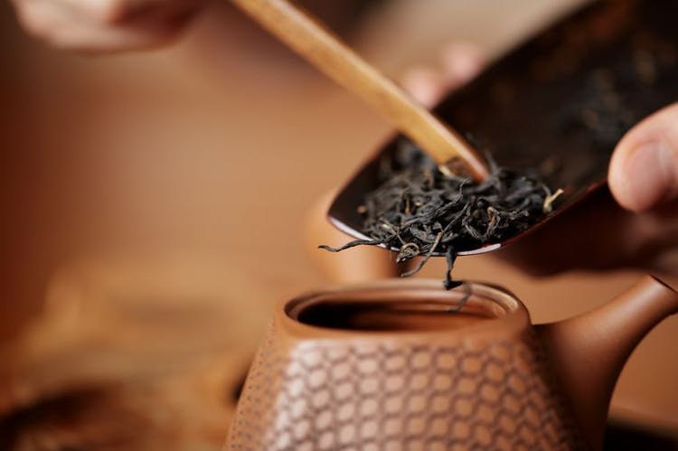 A close-up image of Chinese tea leaves being placed inside a teacup.