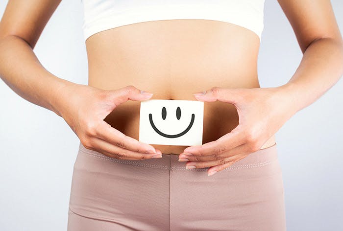 A woman in sports attire holding white cardboard with a smiley face in front of her belly button 