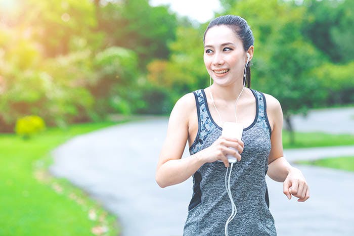 An Asian woman jogging in a park while listening to music from her mobile phone