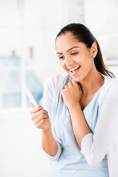 An Asian woman holding a pregnancy test result and looks happy