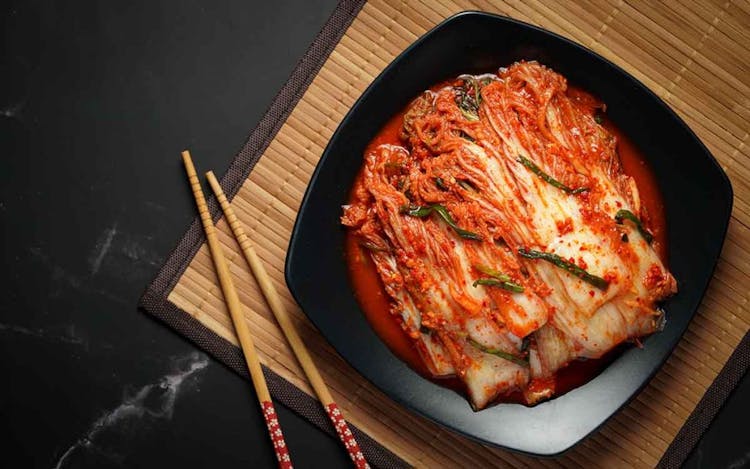 A stack of kimchi served on a black plate with wooden chopsticks on the side