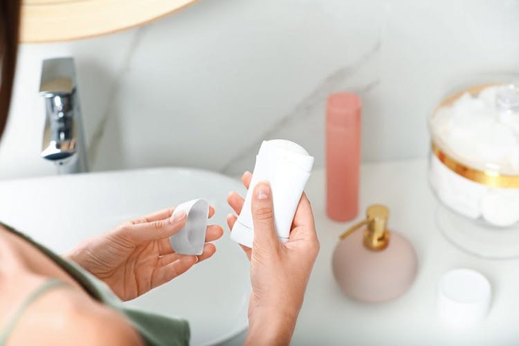 A woman holds an opened deodorant stick in front of her bathroom sink