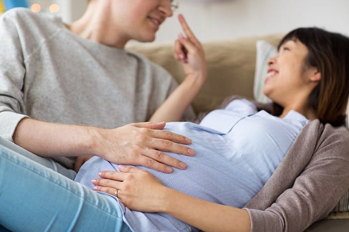A pregnant lady with her partner relaxing and holding the woman’s belly