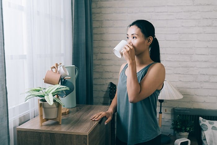 An Asian woman drinking from a mug while looking out of a window