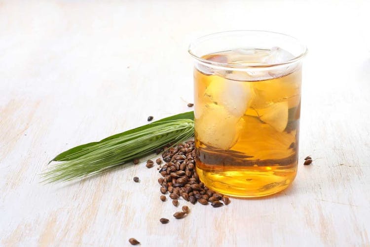 A glass of iced barley tea with roasted barley beans and leaves on a wooden table