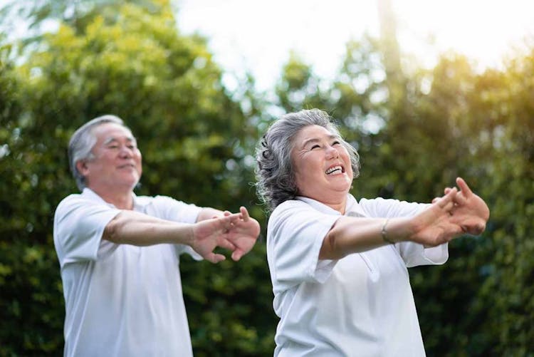 Two elderly Asians in all-white attire doing morning exercises