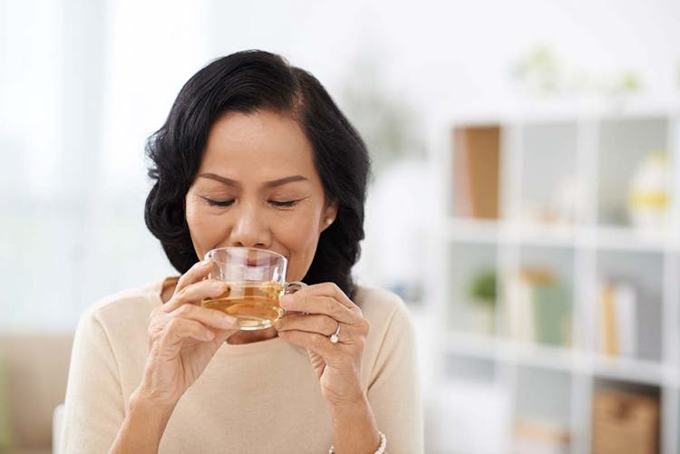 A middle-aged Asian woman drinking tea from a glass cup