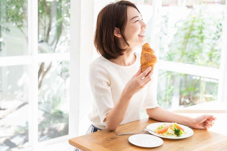 A woman eats a croissant and salad for lunch