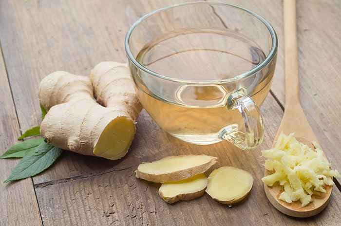 A ginger root, ginger slices, ginger strips, and a glass of brewed ginger tea on a wooden table