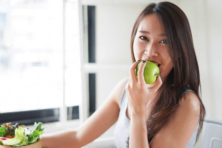 A woman biting a green apple that she is holding in her left hand