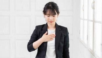 A female executive closes both eyes while placing her right palm on her chest to calm herself down