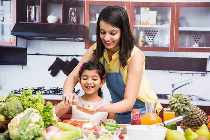 A mom and her daughter preparing food in a kitchen filled with fruits and vegetables