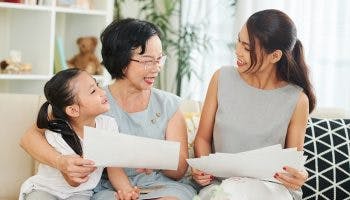 A middle-aged Asian woman sitting on a couch with her daughter and granddaughter, reading papers