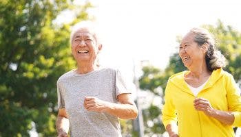 An elderly Asian couple running outdoors with smiles on their faces