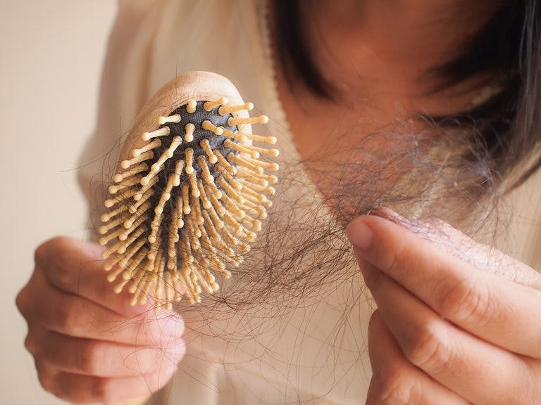 Woman holding strands of hair that are stuck to a brush