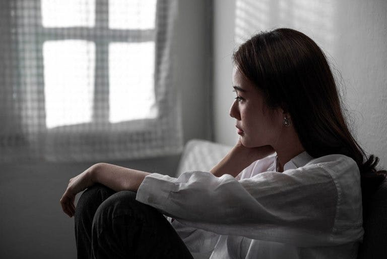 A woman sitting against a wall as she stares into the distance with a gloomy look on her face
