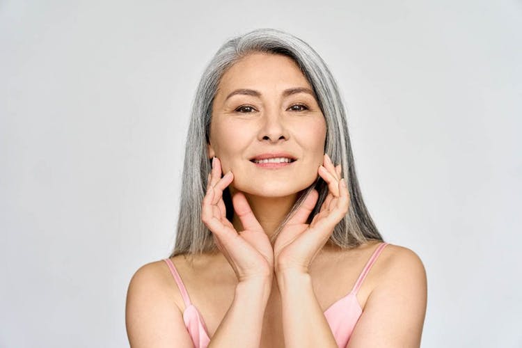 A middle-aged Asian woman giving herself a facial massage with her fingers