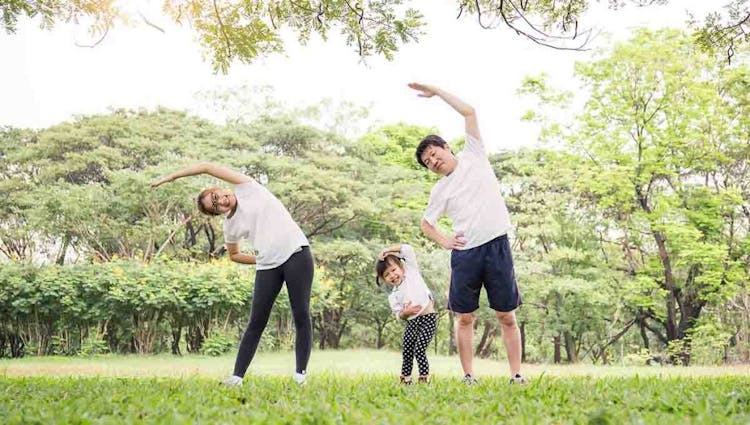 An Asian man, woman and young daughter exercise together in a park